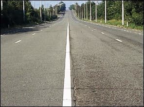 Photo d'une route large aux bandes multiples, séparée en son milieu par une ligne blanche continue ; pas de berme centrale visible.
