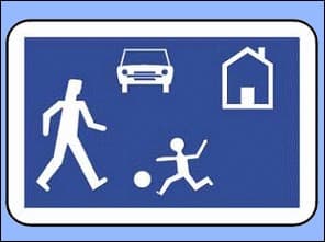Photo agrandie d'un panneau bleu de zone résidentielle : une voiture, une maison, un piéton, un enfant qui joue au ballon.