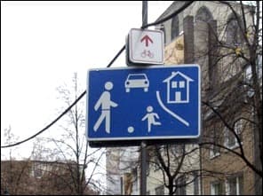 Photo d'un panneau bleu de zone résidentielle fixé sur un poteau, surmonté d'un petit panneau rouge et blanc avec une flèche et un vélo.