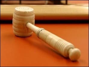 Photo d'un marteau de juge en bois posé sur une table, sur fond orange.