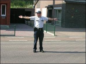 Photo d'un agent de police debout devant un garage, les deux bras tendus à l'horizontale.