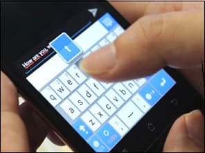 Photo d'une main qui écrit un message sur l'écran d'un smartphone, clavier affiché.