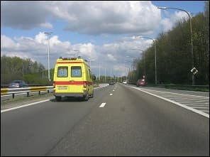Photo d'une autoroute : une ambulance jaune roule au premier plan, d'autres voitures circulent au loin.